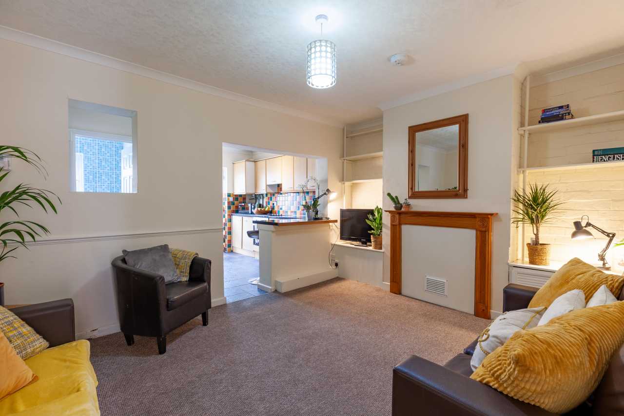 Furnished living room with sofas, armchairs, a fireplace, shelving and an open kitchen area.
