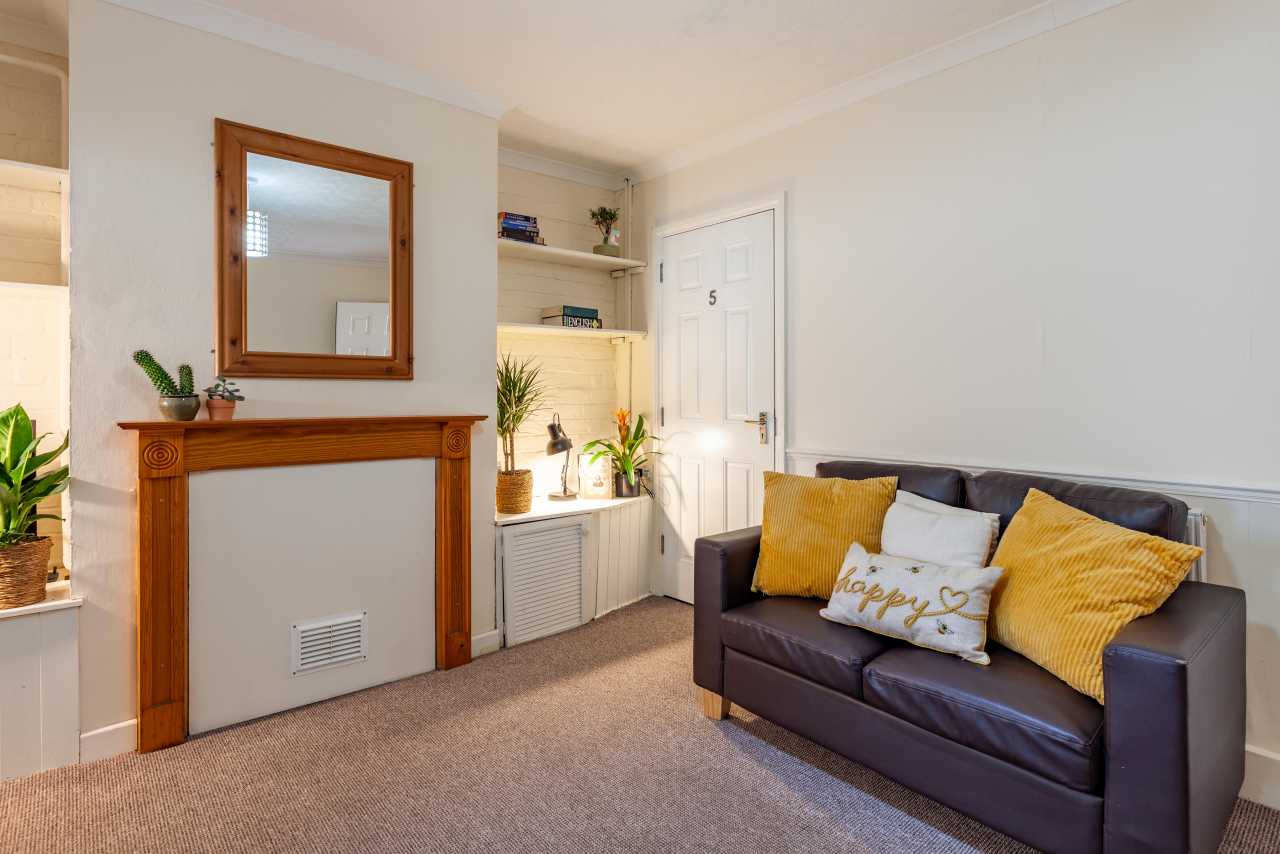 Furnished living room with a dark sofa, yellow cushions, fireplace surround, built-in shelving and carpeted floor.