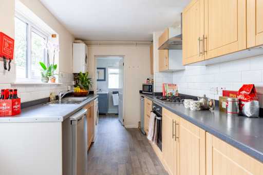 A bright galley-style kitchen with wooden cabinets, gray countertops, appliances, a sink, and a rear doorway.