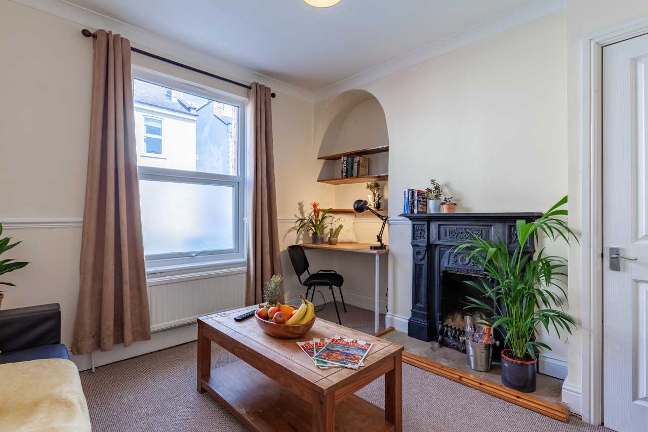 Bright sitting room with a window, curtains, fireplace, desk, plants and a coffee table.