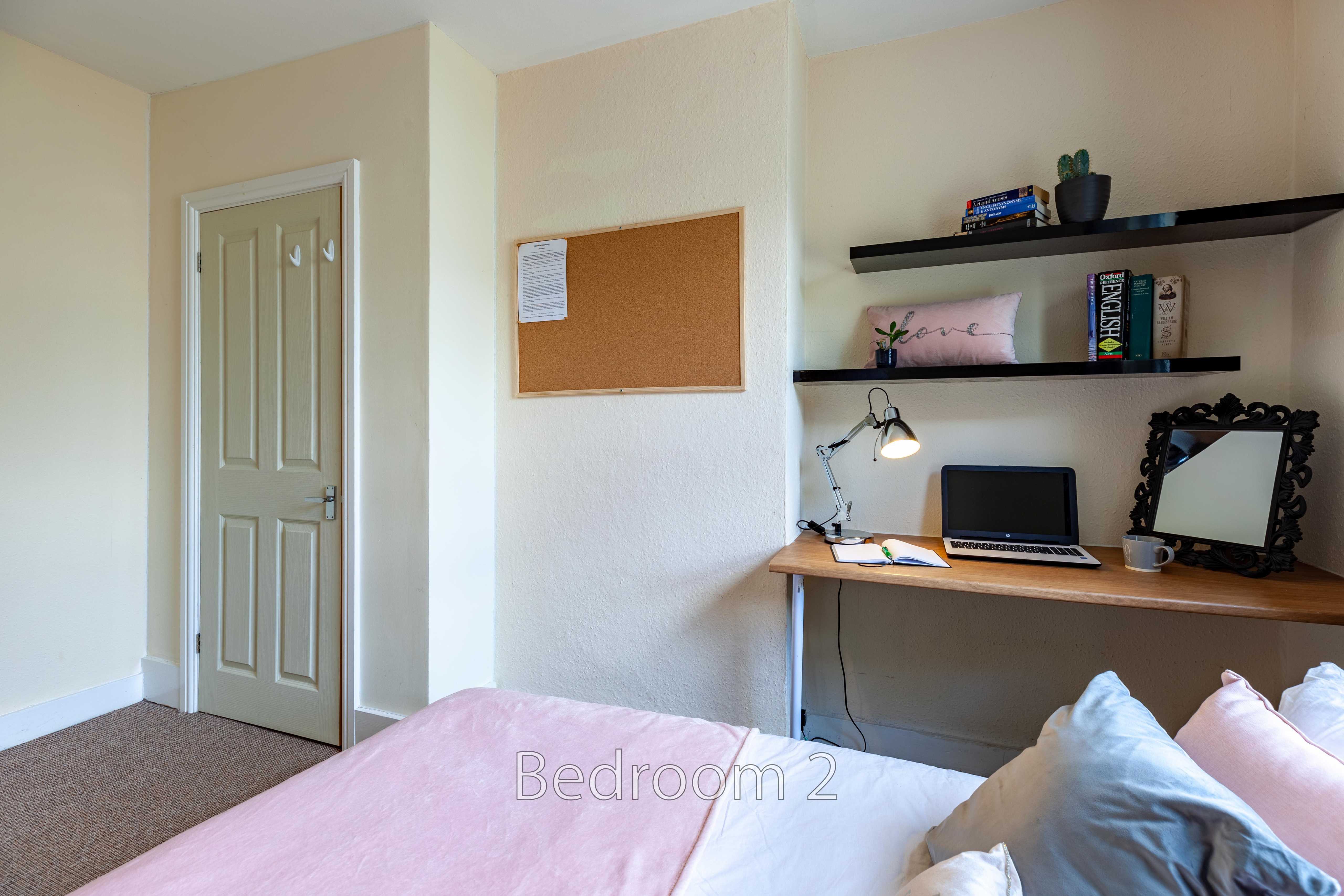 A bedroom with a bed, desk, computer, shelves, mirror and closed door.