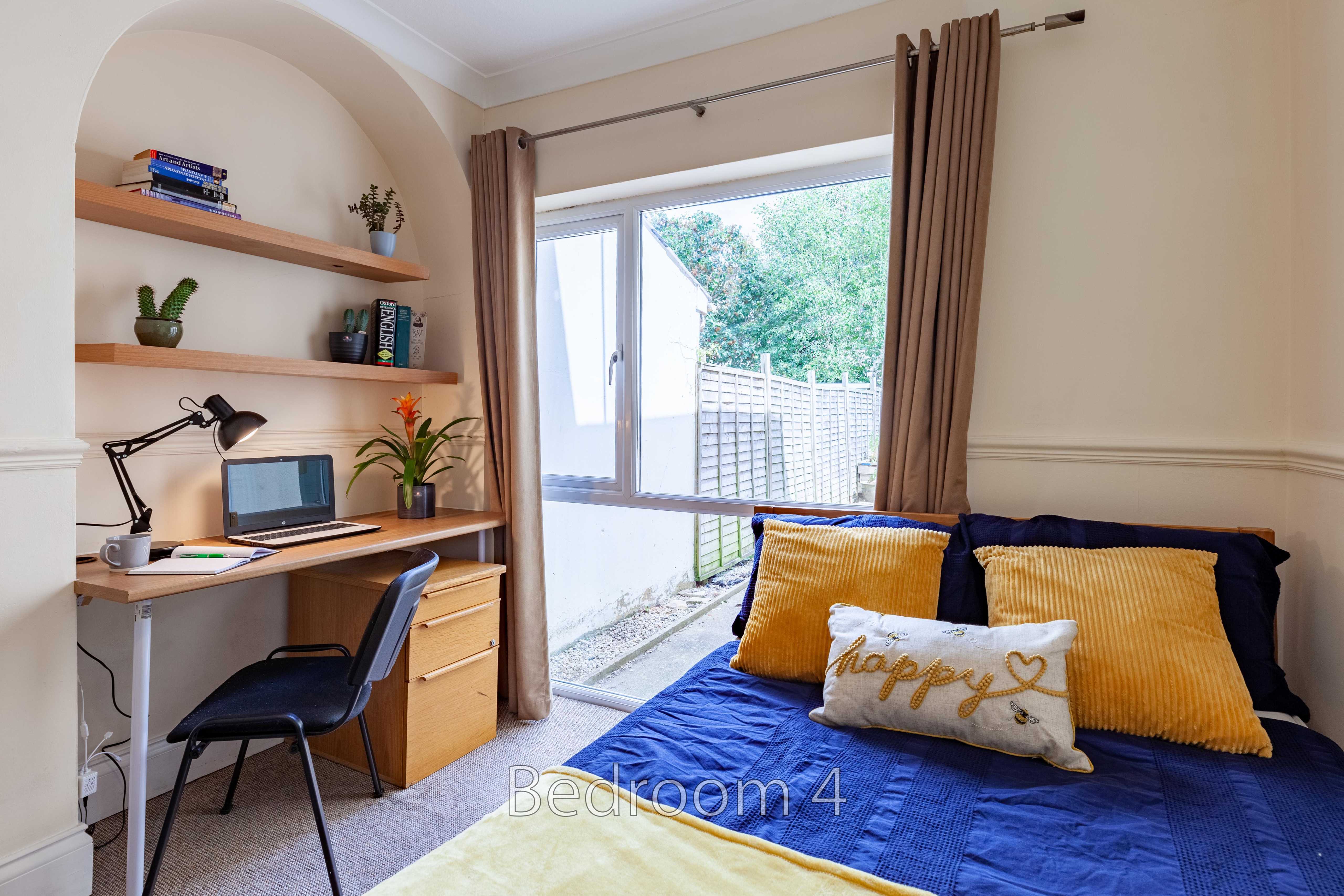 Bedroom with a double bed, desk, chair, wall shelves, curtains and a glass door opening to a small outdoor area.