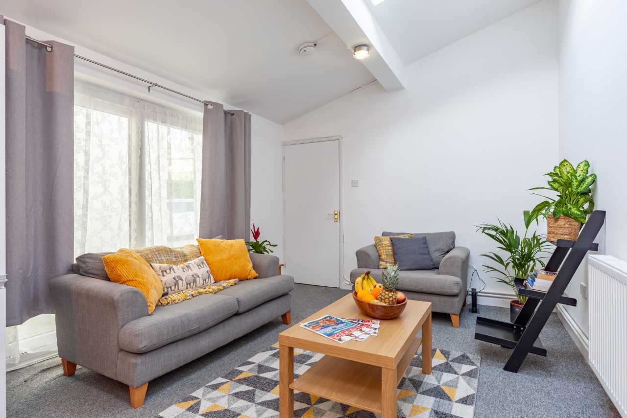 Furnished living room with grey sofas, a wooden coffee table, patterned rug, curtains, plants and a radiator.