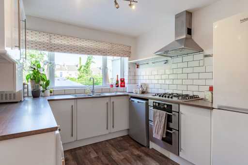 Bright fitted kitchen with white cabinets, a gas hob and oven, stainless steel extractor hood, sink, dishwasher and window.