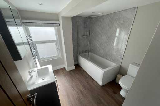 Modern bathroom with a bathtub, toilet, sink, mirrored cabinet and wood-effect flooring.