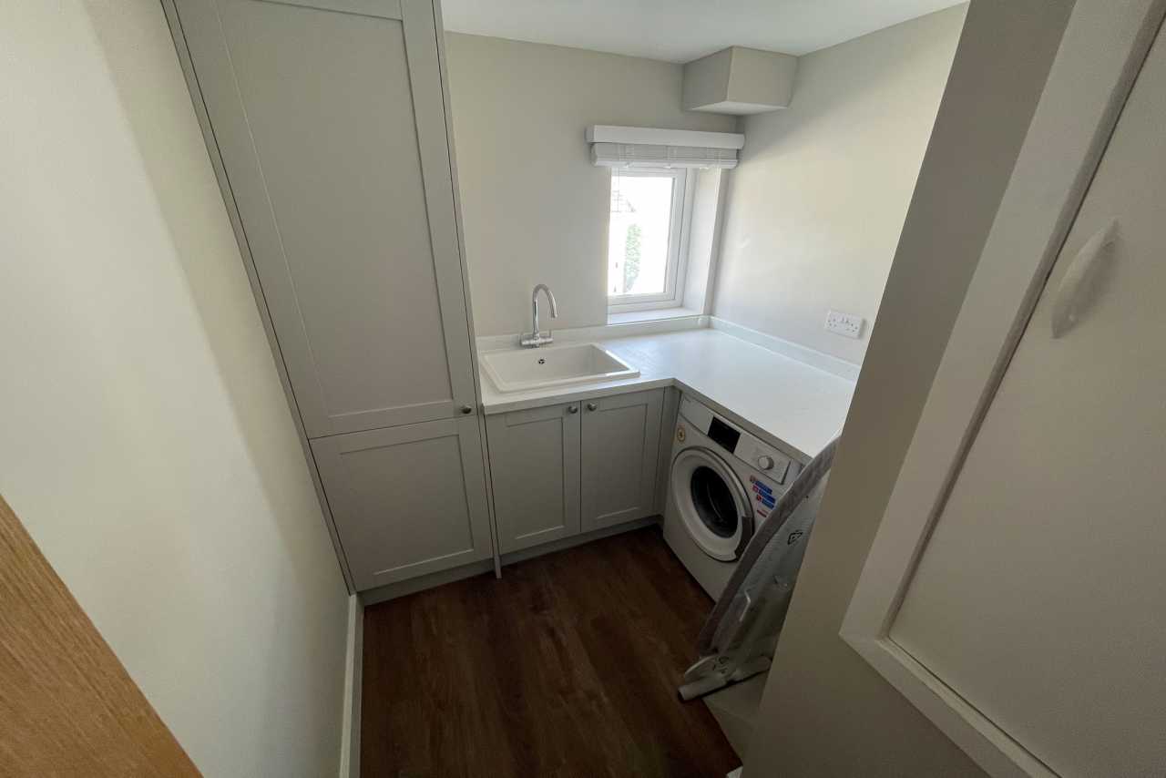 Compact utility room with cabinets, sink, washing machine, countertop and window.