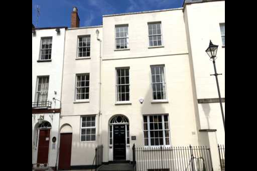 White-painted multi-storey terraced residential building with black railings, several sash windows, and front doors.