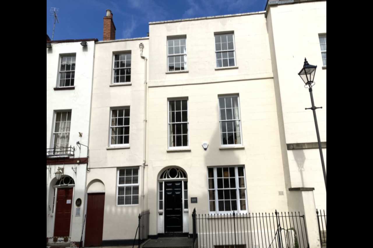 White-painted multi-storey terraced residential building with black railings, several sash windows, and front doors.