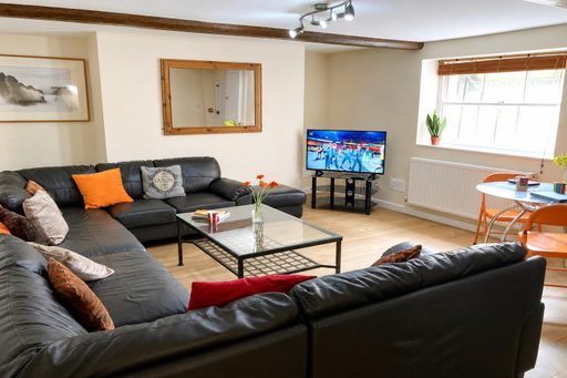 A furnished communal living room with sofas, a coffee table, television, dining table and windows.