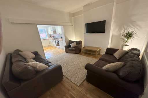 Living room with sofas, armchair, wall-mounted television, coffee table and doorway to a kitchen.