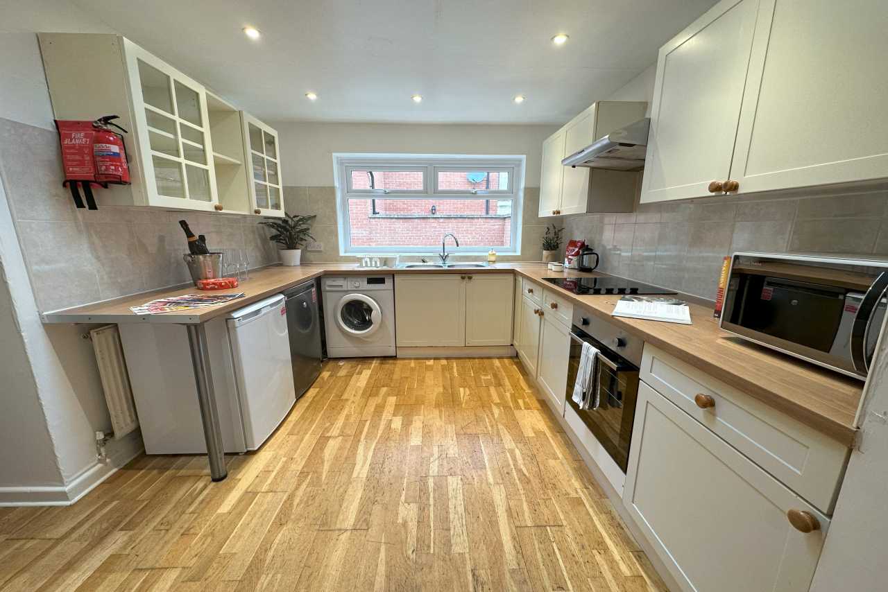Bright fitted kitchen with wooden flooring, white cabinets, appliances and a window.
