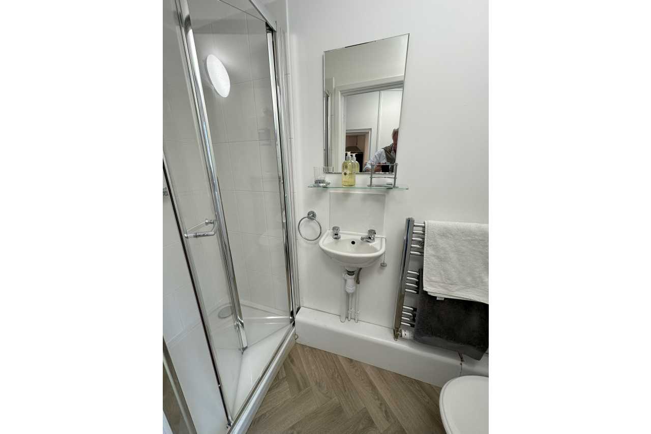 A compact bathroom with a glass shower enclosure, pedestal sink, wall mirror, heated towel rail and partial view of a toilet.