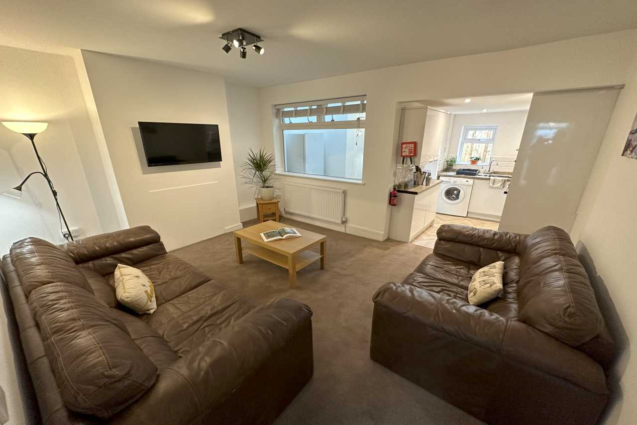 Living room with two brown sofas, a coffee table, wall-mounted television, window and open view into a kitchen.