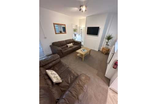 A furnished living room with two brown sofas, a coffee table, wall-mounted television, carpet and houseplants.