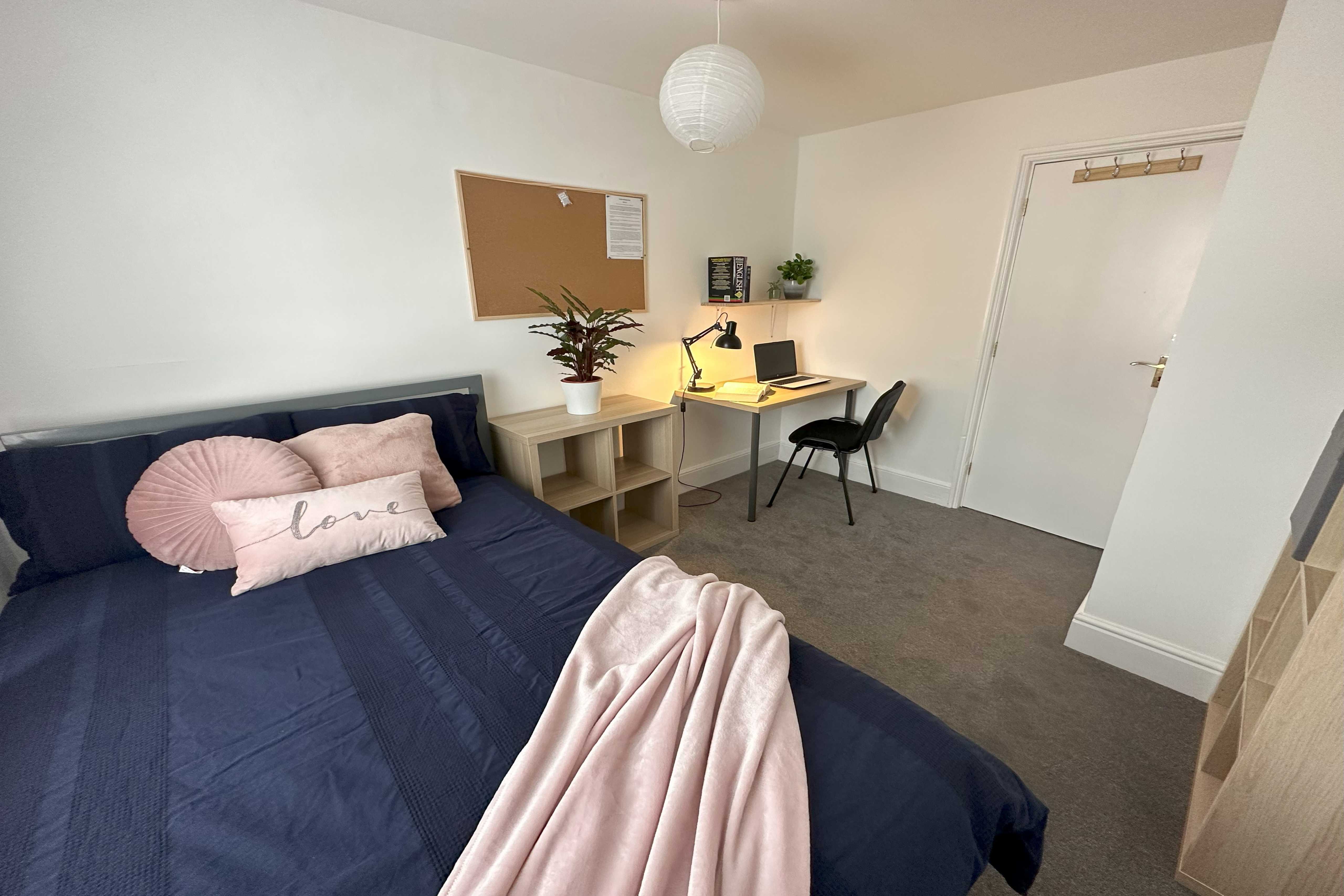 A furnished bedroom with a double bed, desk, chair, wardrobe and window.