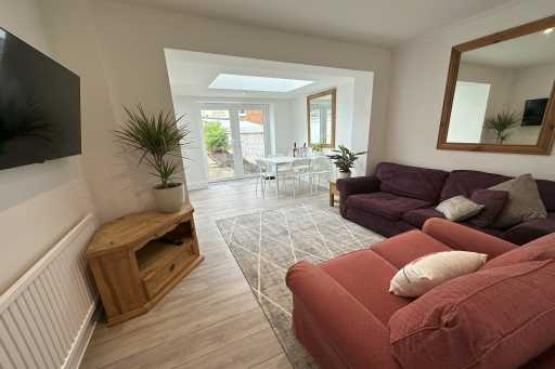 Living room with sofas, television, wooden cabinet and a dining area visible through a wide opening.