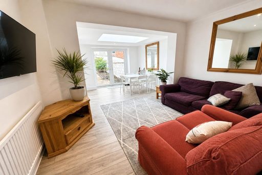 Living room with sofas, television, wooden cabinet and a dining area visible through a wide opening.