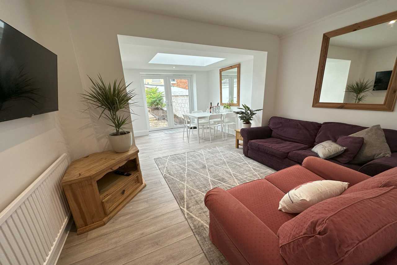 Living room with sofas, television, wooden cabinet and a dining area visible through a wide opening.