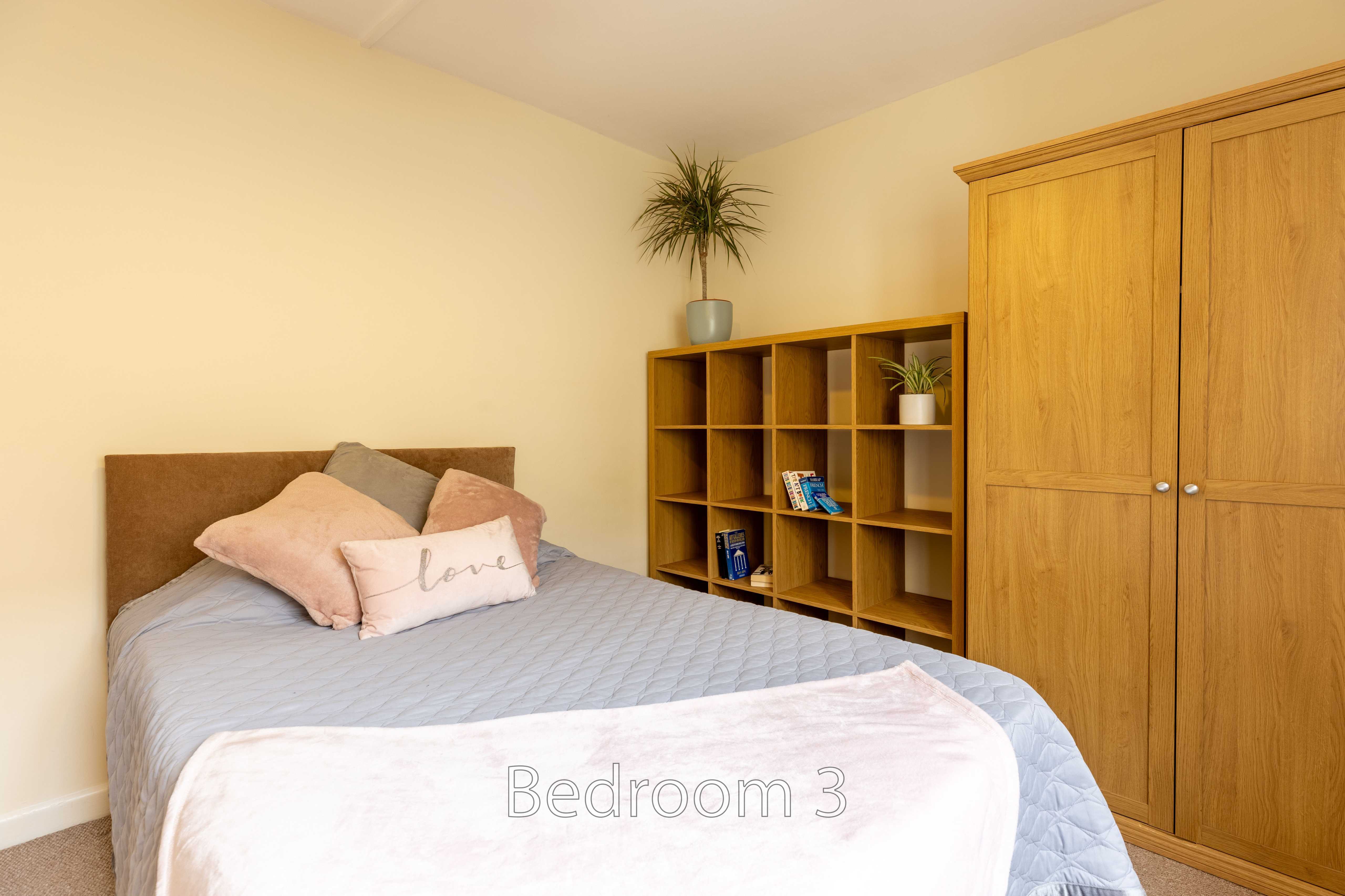 A bedroom with a single bed, pillows, wooden shelving, and a built-in wardrobe.