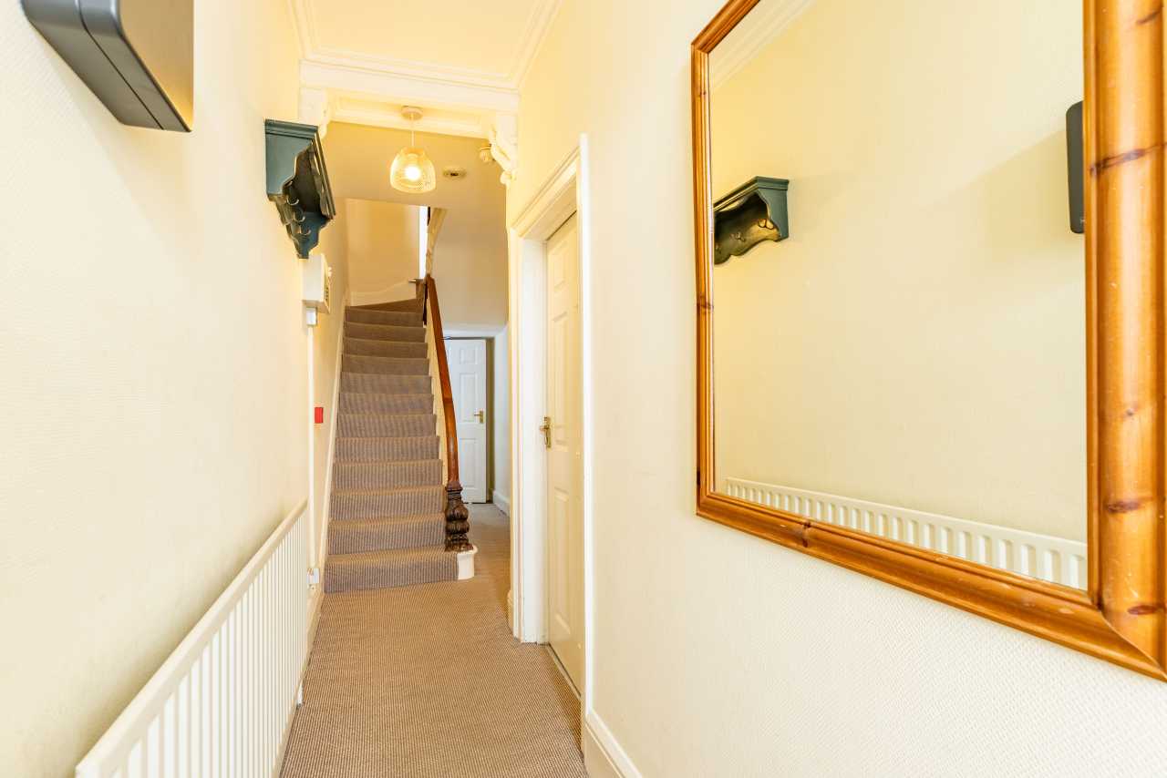 A carpeted hallway with a staircase, radiator, wall mirror and several doors.