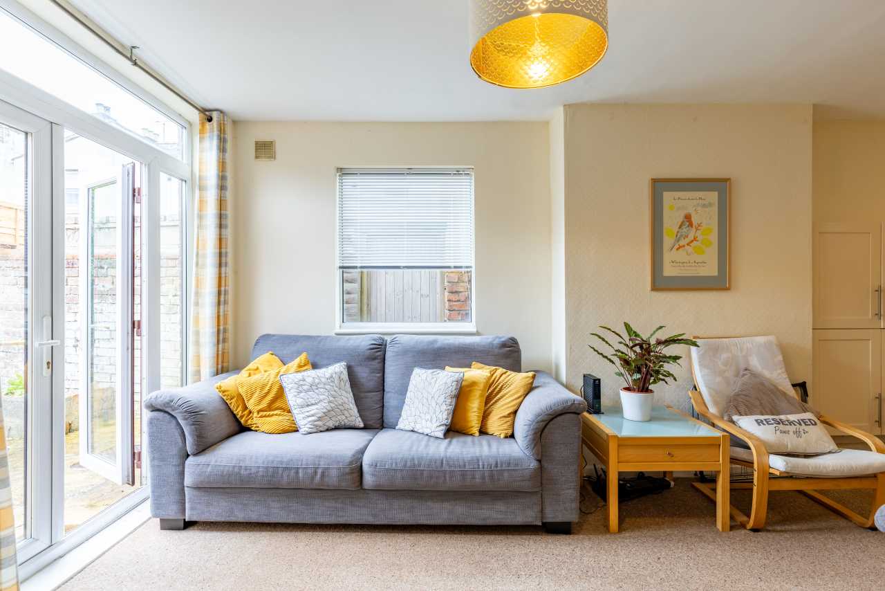 Bright living room with a grey sofa, armchair, coffee table, large windows and a glass door.