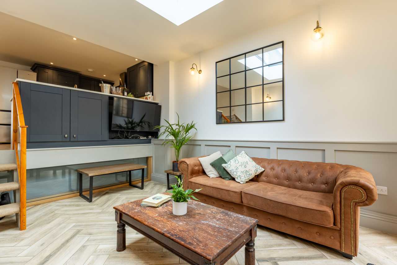 Furnished living room with a brown sofa, coffee table, wall-mounted television and open kitchen area.