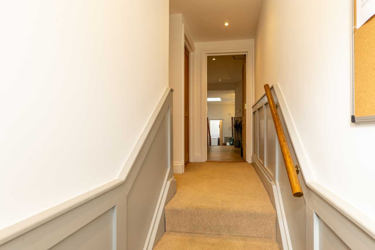 Carpeted staircase and hallway with white walls, wood trim, and handrails.