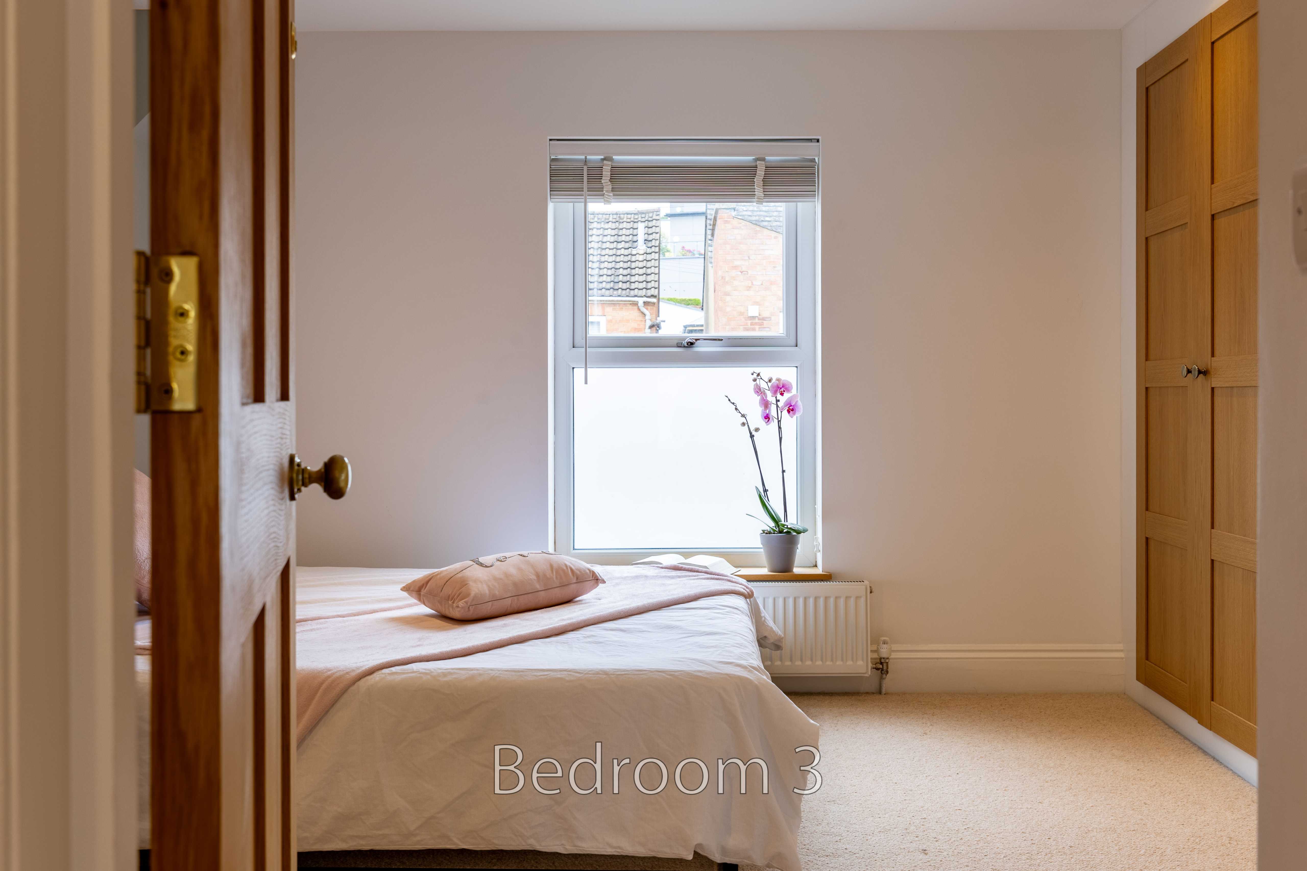 A furnished bedroom with a double bed, window, radiator, wardrobe and carpeted floor.