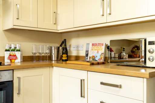A bright fitted kitchen with cream cabinets, wooden worktops, a microwave, sink area and kitchen items on the counters.