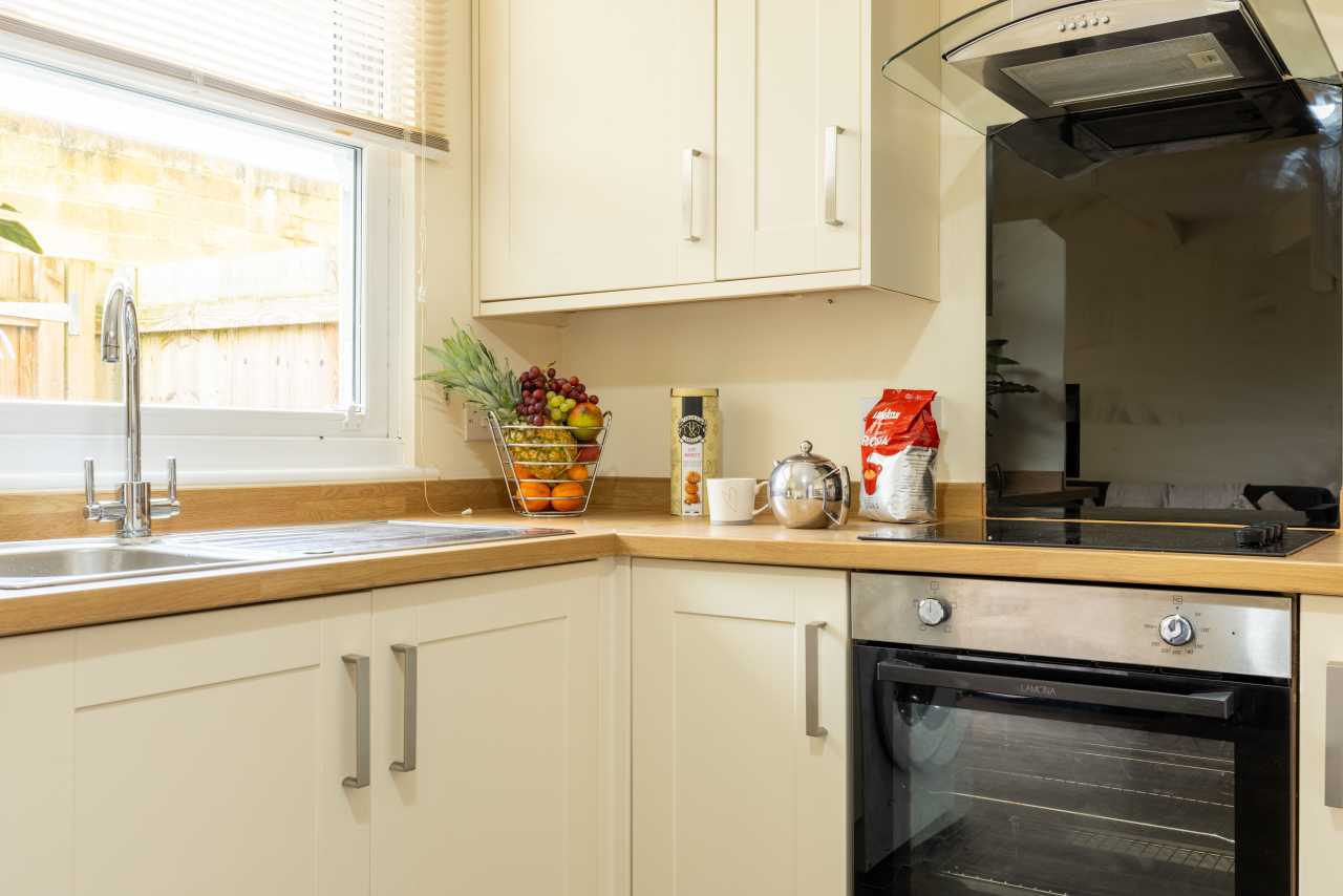 Bright fitted kitchen with cream cabinets, wooden worktops, a sink beneath a window, and a built-in oven and hob.