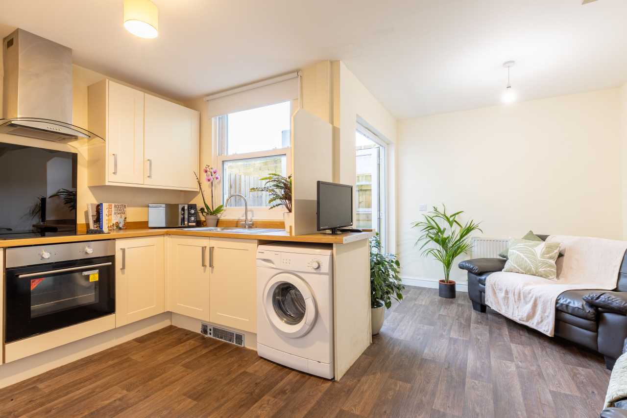 Open-plan kitchen and living area with fitted cabinets, appliances, dining counter, sofa and plants.
