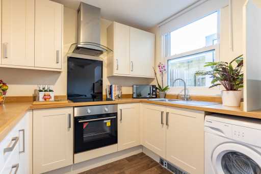 A bright fitted kitchen with cream cabinets, wooden worktops, an oven, sink, appliances and a washing machine.