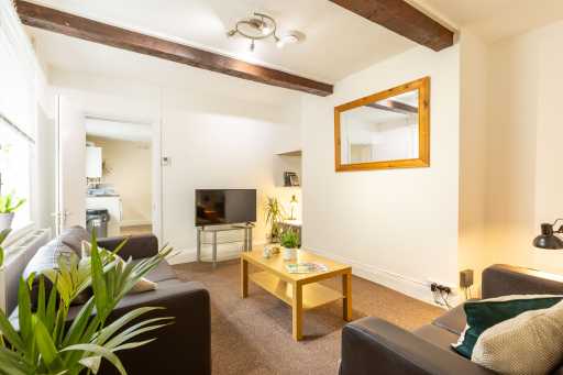 Bright living room with sofas, a coffee table, television, wall mirror, plants, and exposed ceiling beams.