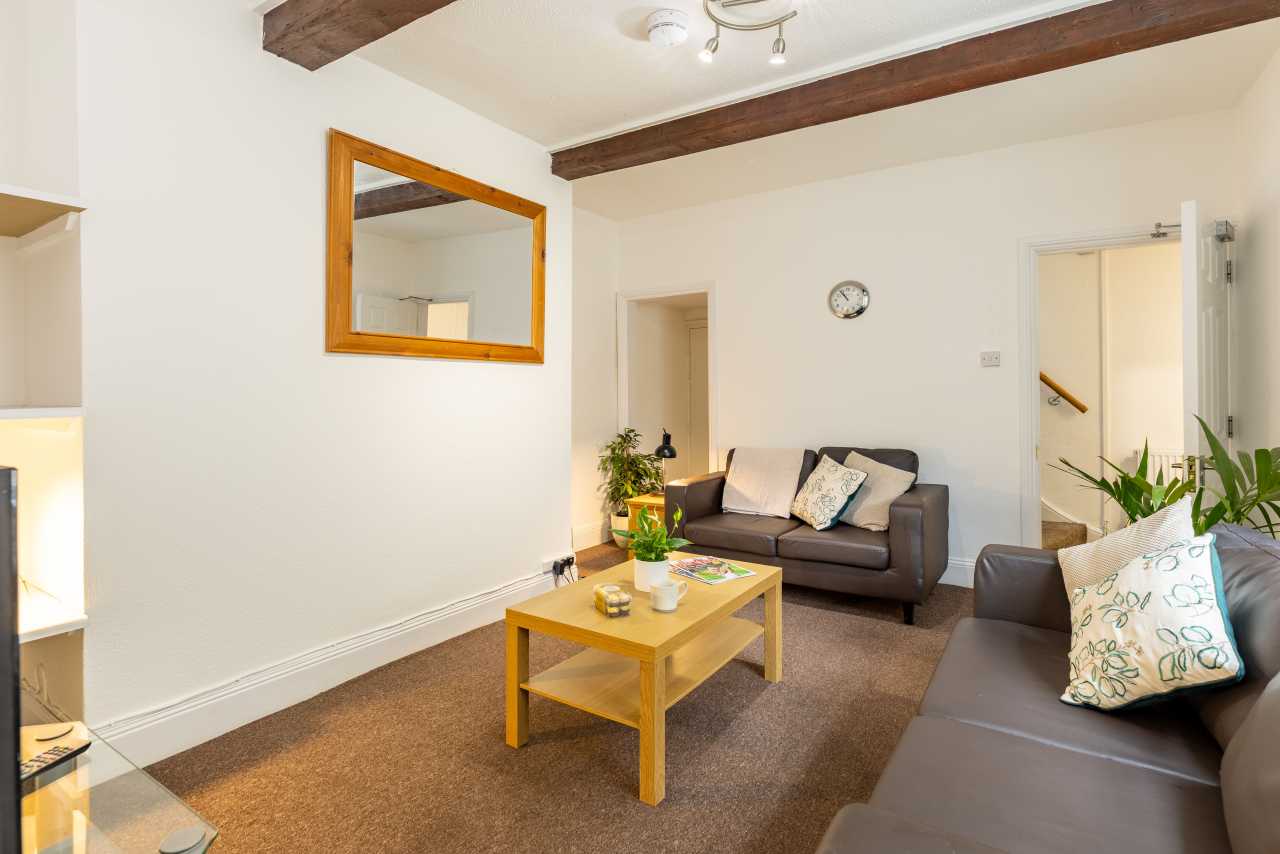 A furnished living room with two sofas, a coffee table, wall mirror, exposed ceiling beams and doorways.