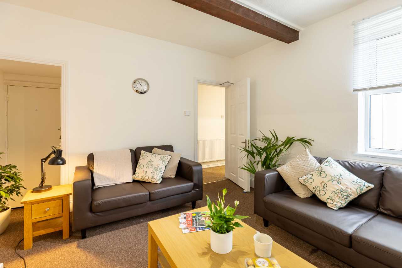 A bright furnished living room with two dark sofas, a wooden coffee table, plants, a side table and a window with blinds.