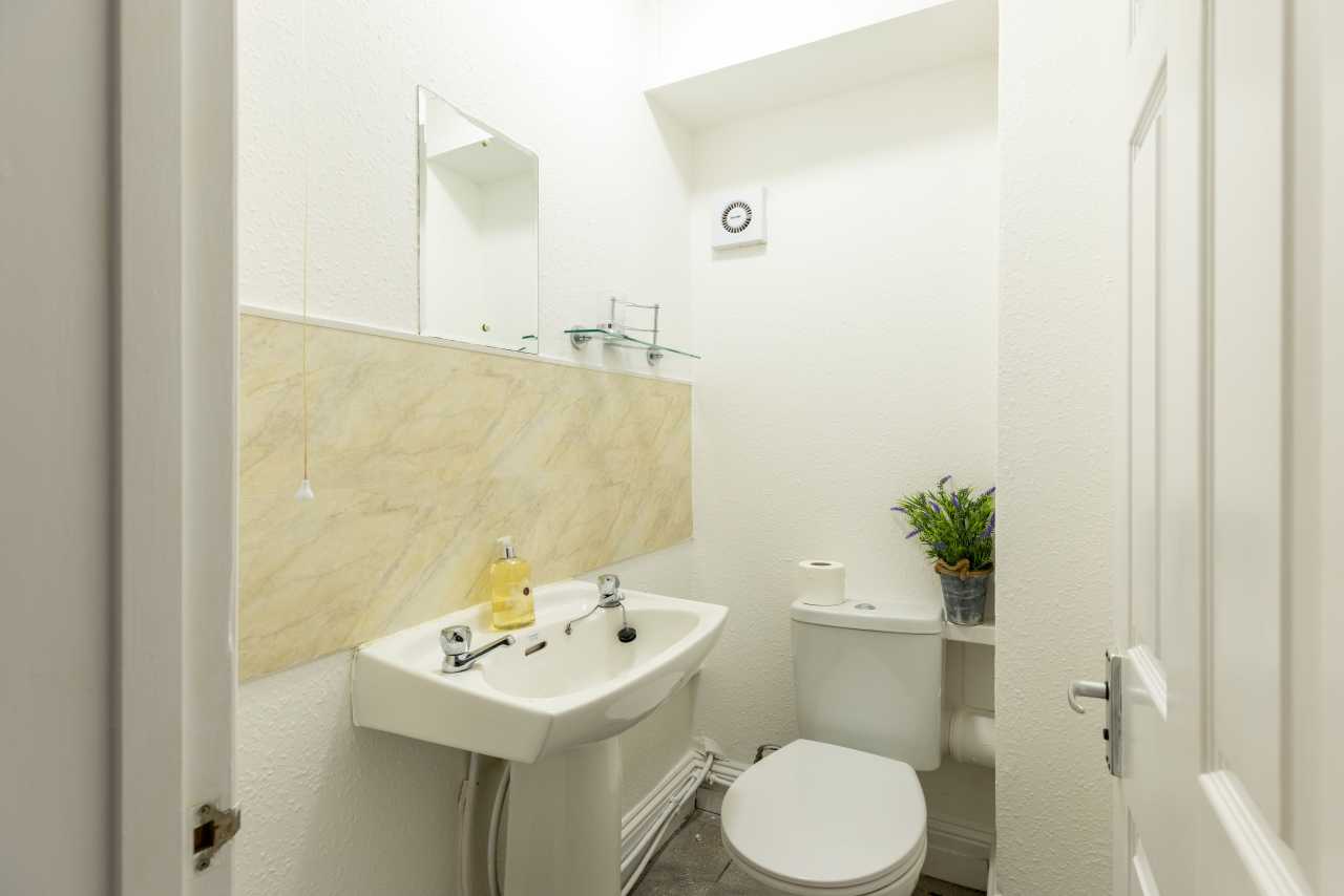 Small white bathroom with a sink, toilet, mirror, tiled backsplash and potted plant.