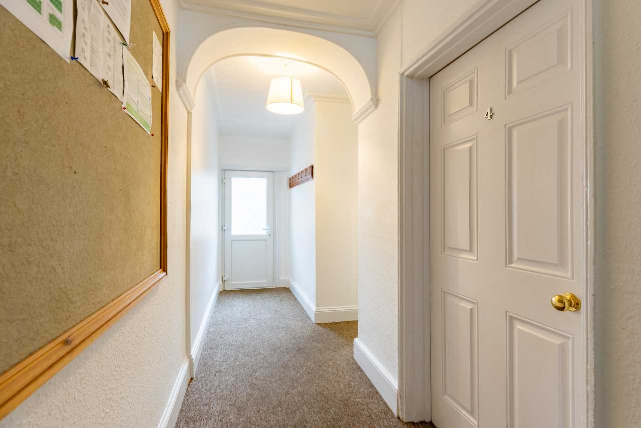 Interior hallway with carpeted floor, an arched opening, a closed paneled door, a bulletin board, and an exterior door at the far end.