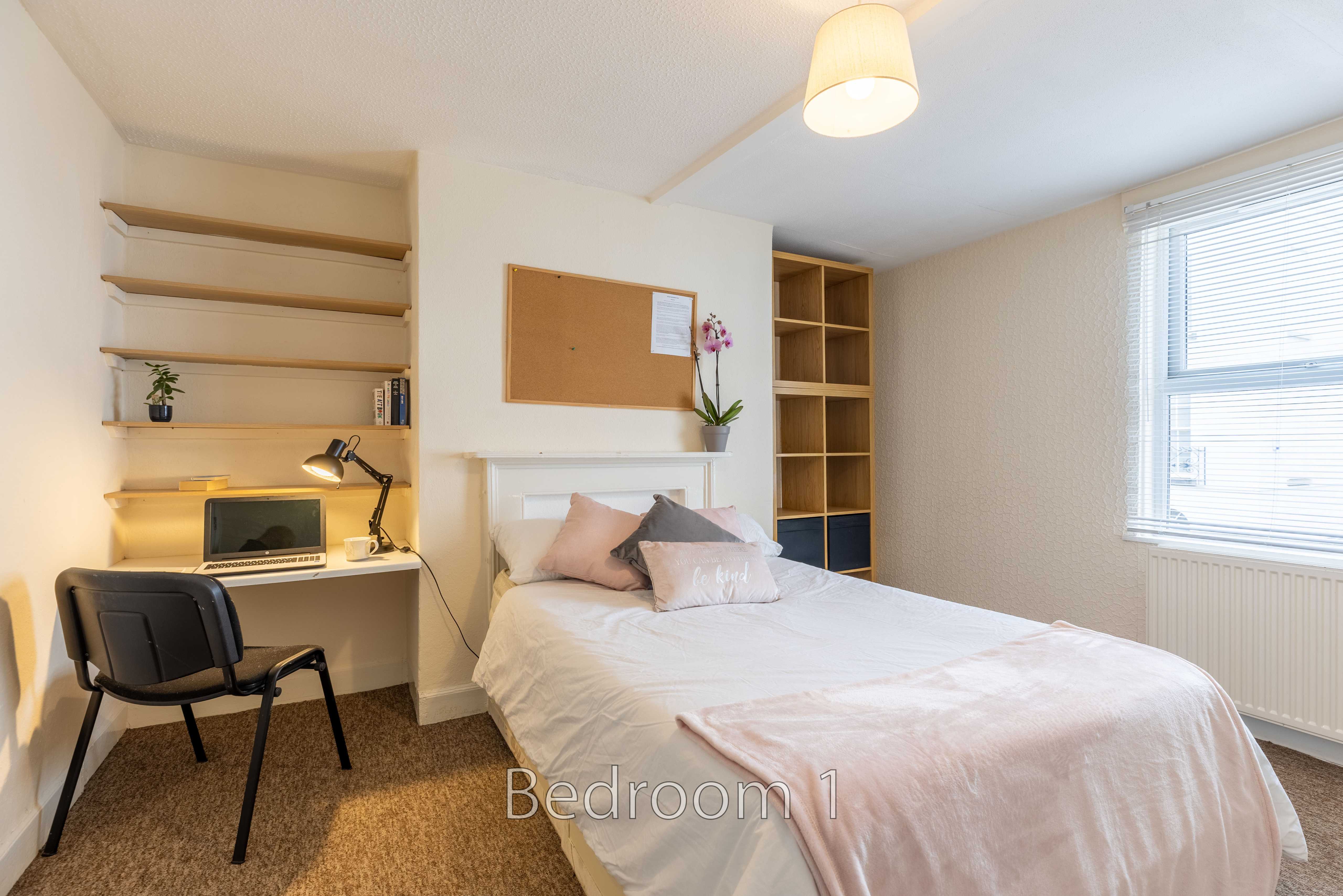 A furnished bedroom with a single bed, desk, chair, shelves, wardrobe, window and radiator.