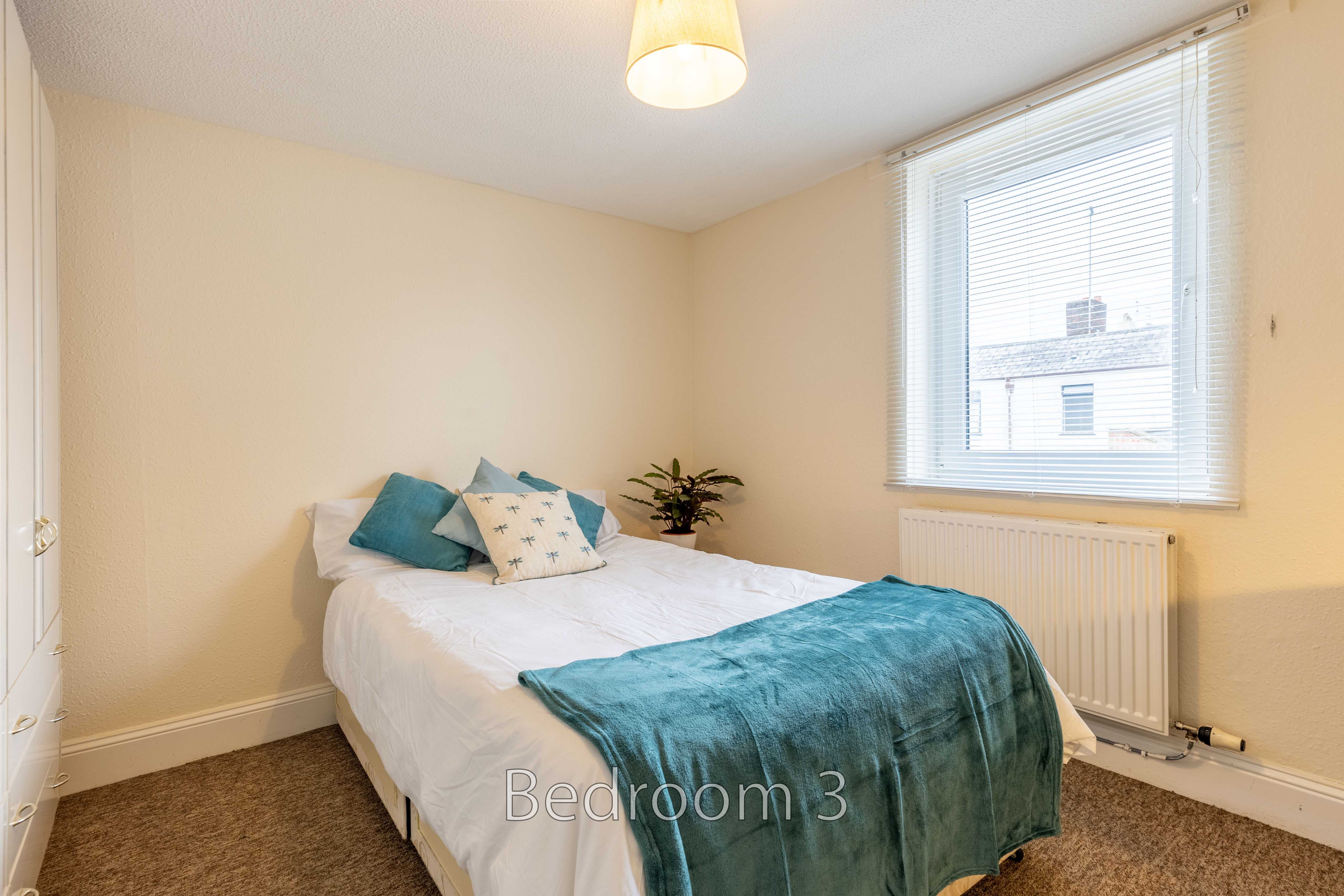 A furnished bedroom with a single bed, blue bedding, a window with blinds, and a radiator.
