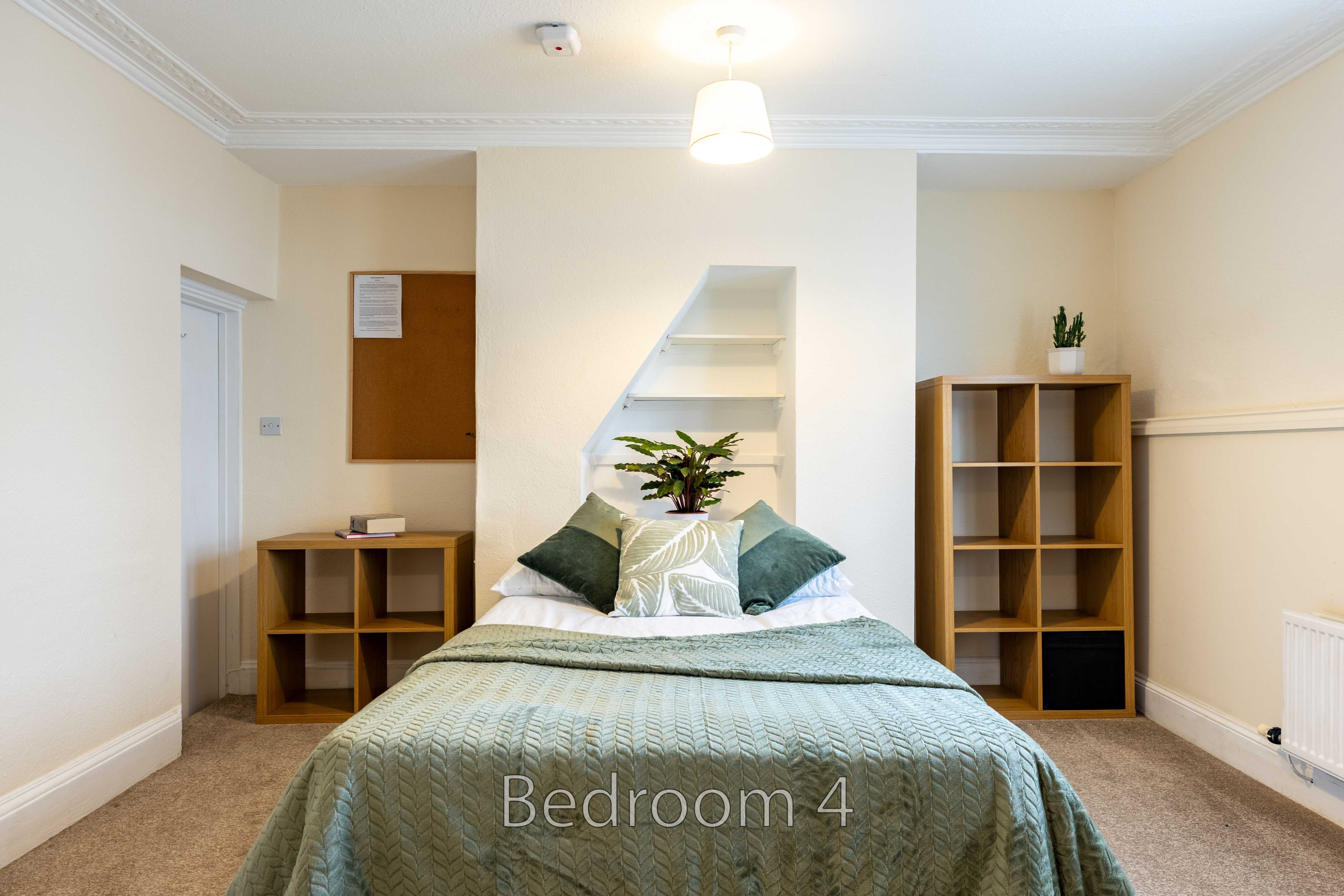 A bedroom with a double bed, bedside furniture, shelving, wall lighting and a radiator.