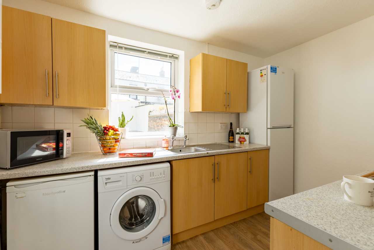 A fitted kitchen with wooden cabinets, a countertop, sink, microwave, washing machine, dishwasher and refrigerator.