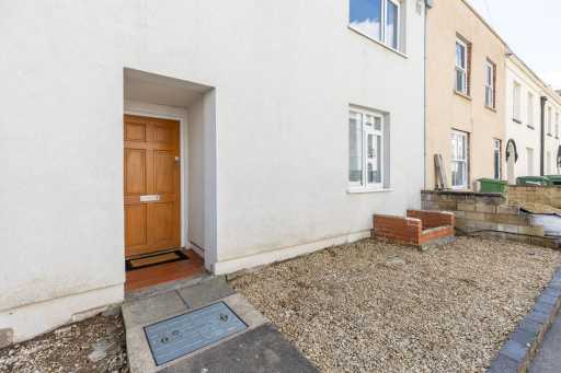Row of attached homes with a wooden front door, gravelled front garden and paved path.