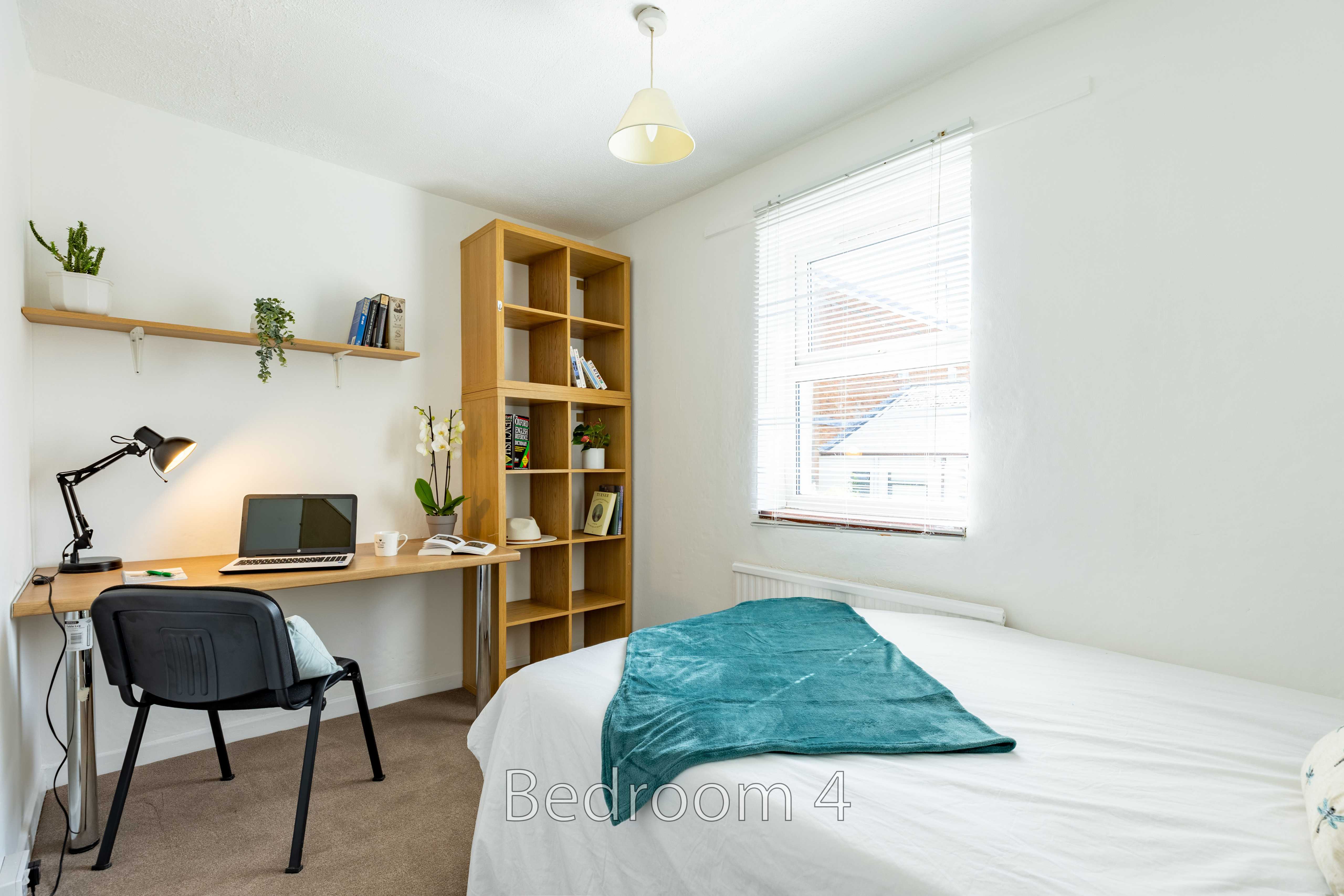A bedroom with a single bed, desk and chair, shelving, and a window with blinds.