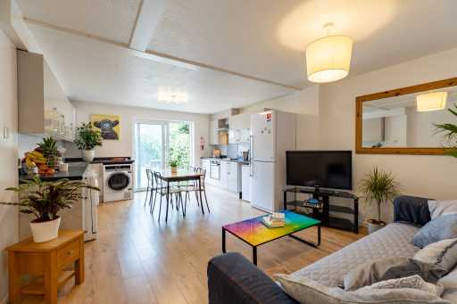 Open-plan living and dining area with a kitchen, sofa, television, dining table and plants.