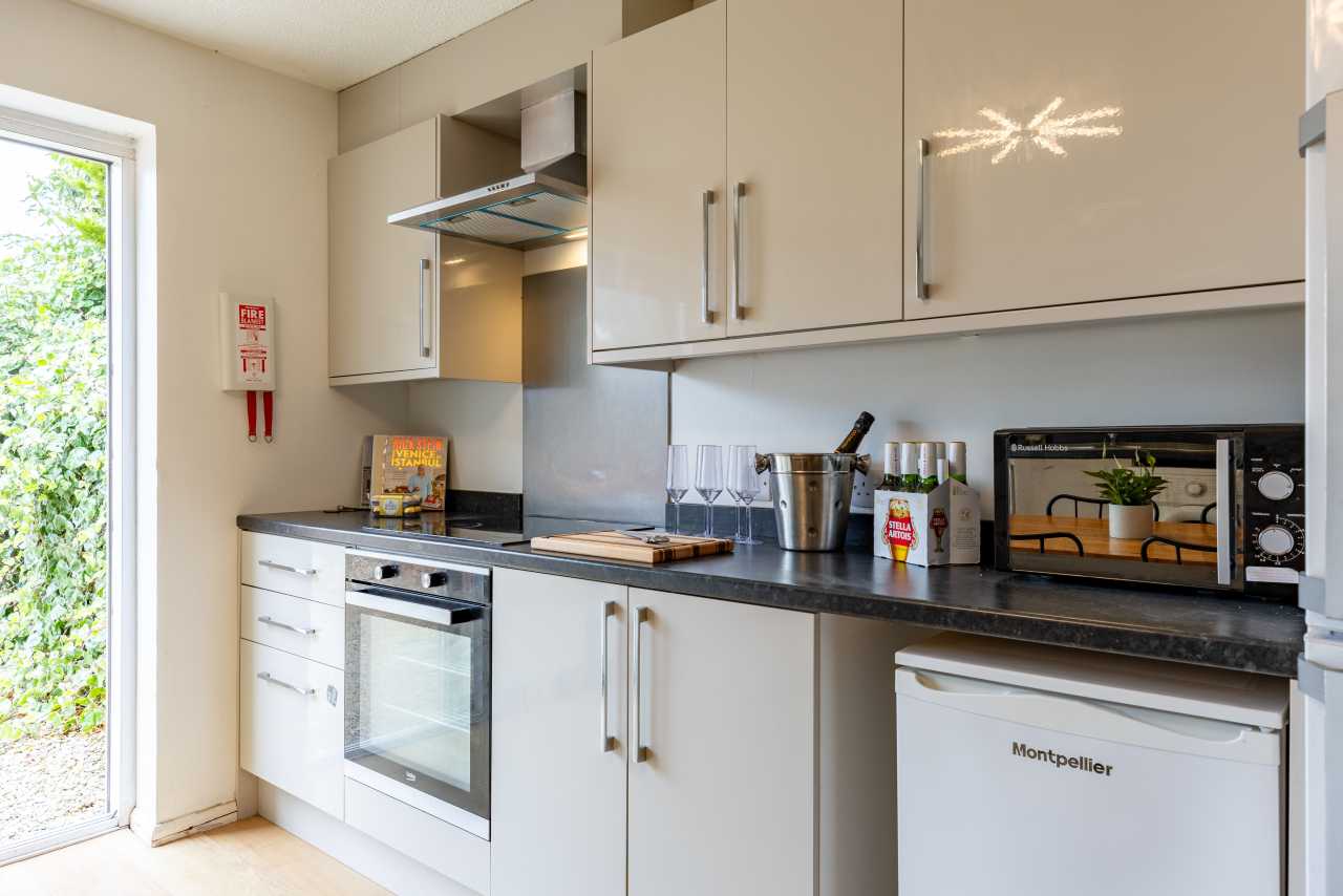 A bright fitted kitchen with white cabinets, a cooker, countertop appliances, and a dishwasher.