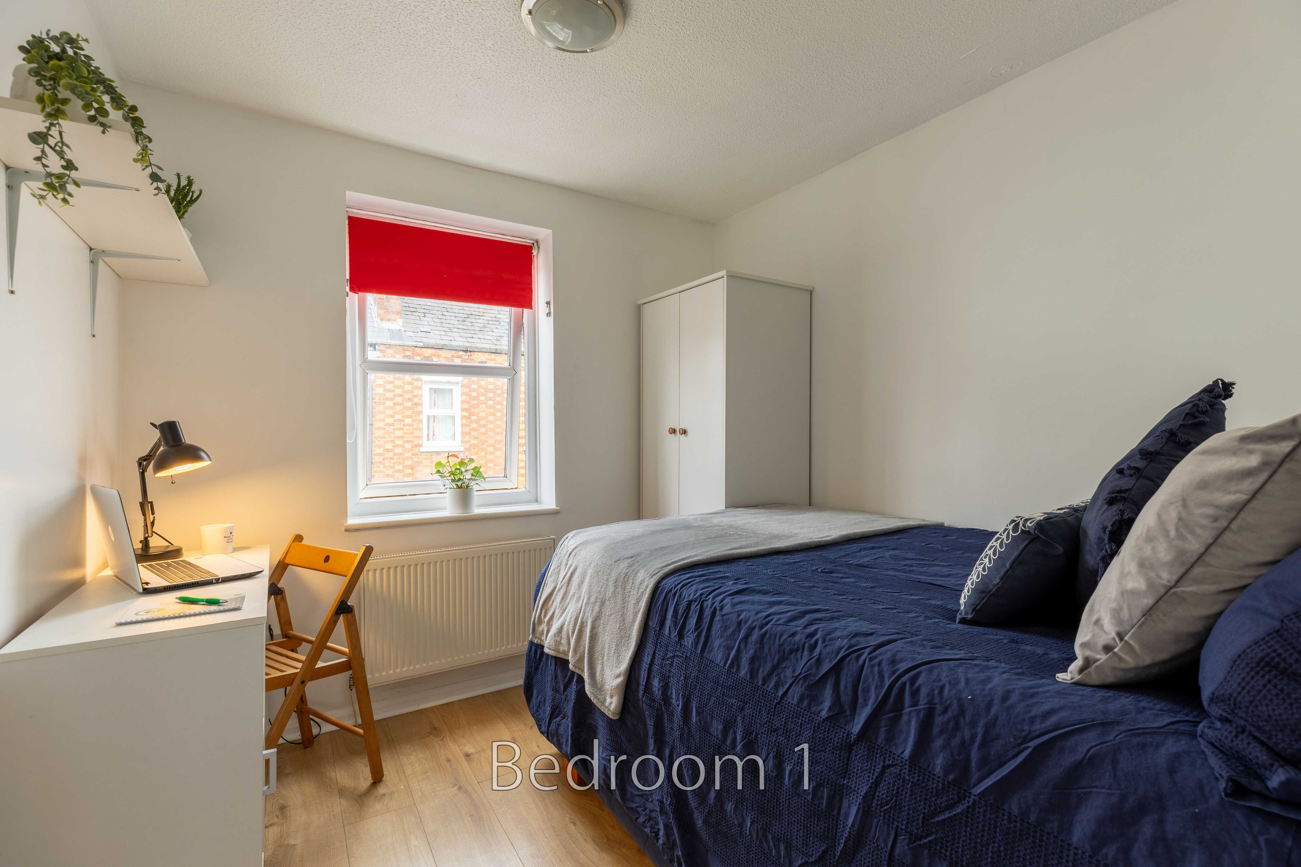 A furnished bedroom with a bed, desk, chair, wardrobe, window and radiator.
