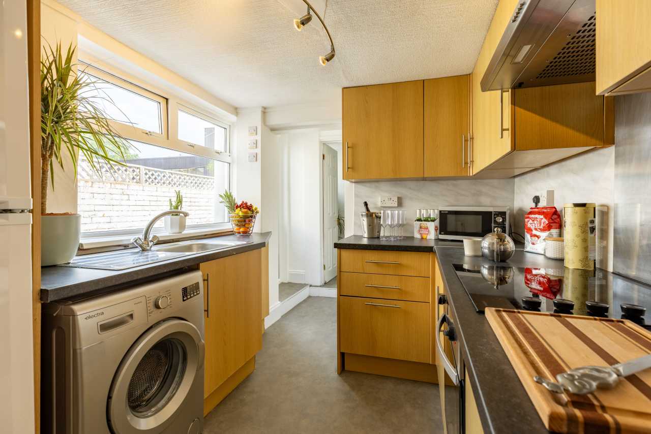 A compact fitted kitchen with wooden cabinets, countertops, sink, washing machine, cooker and microwave.