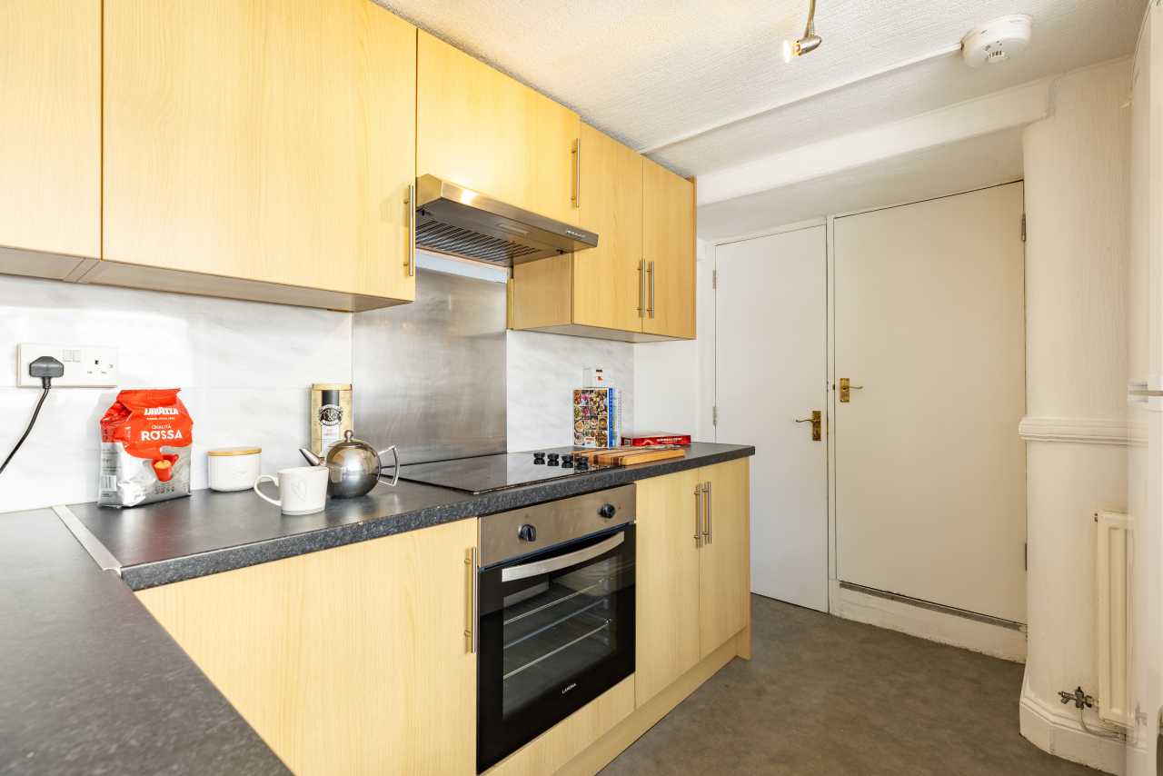 A compact fitted kitchen with wooden cabinets, a countertop, hob, oven, sink and refrigerator space.