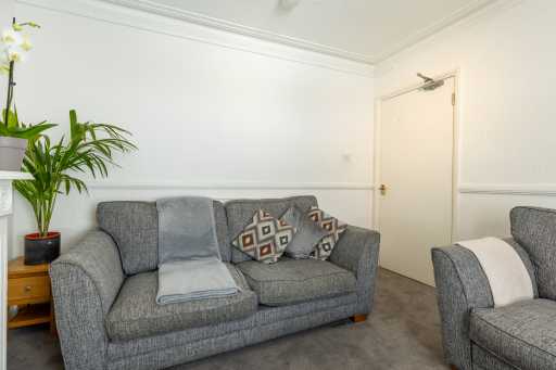 A furnished living room with grey sofas, patterned cushions, a small side table, a potted plant and a closed door.