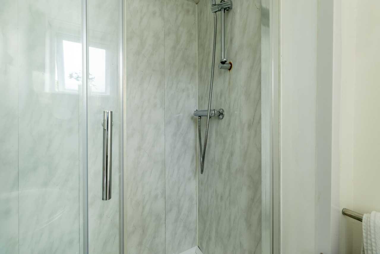 A glass-enclosed shower with marble-effect wall panels, shower fixtures and a towel rail.